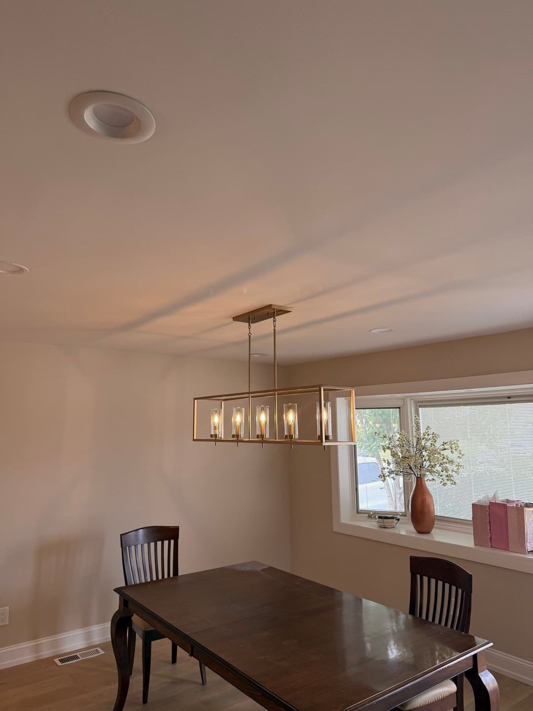 Modern dining room with a stylish chandelier above a wooden table and decorative window.