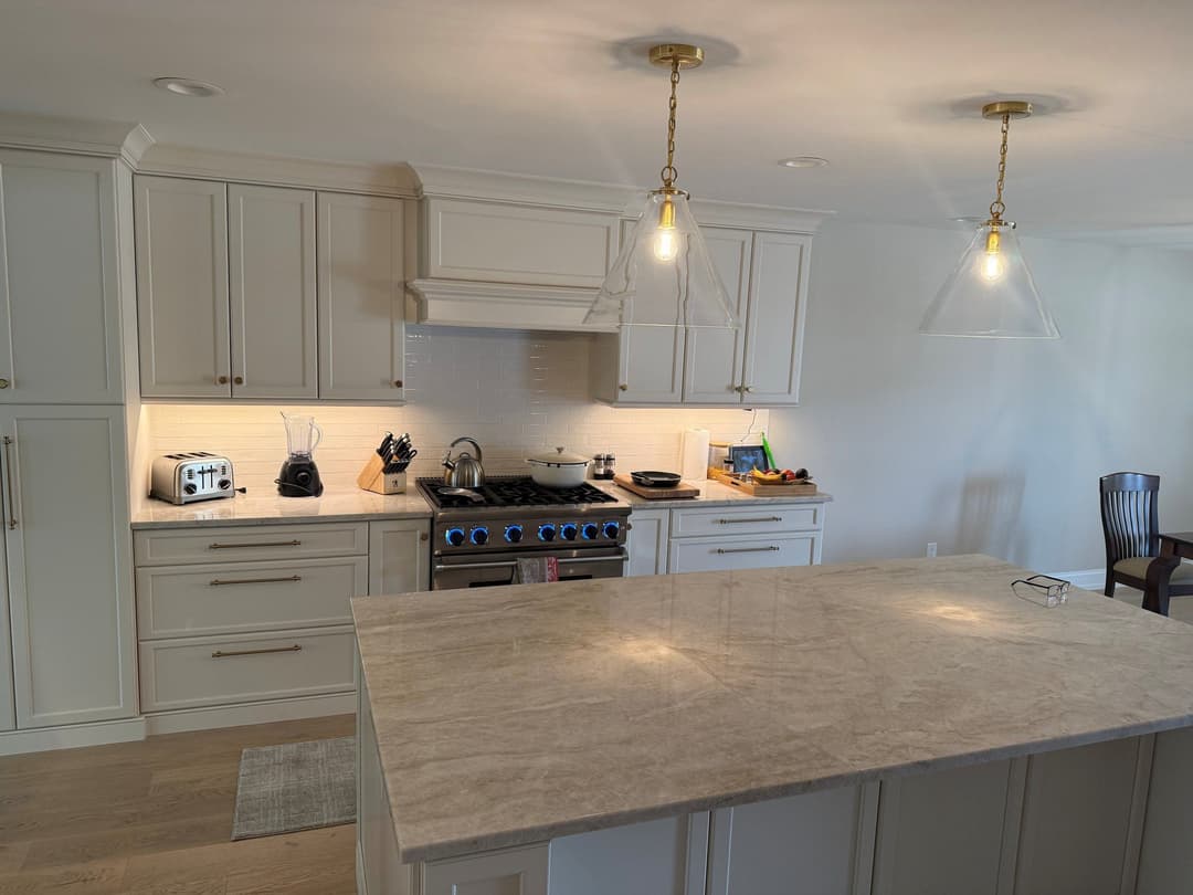 Modern white kitchen with marble island, stainless steel appliances, and elegant pendant lights.