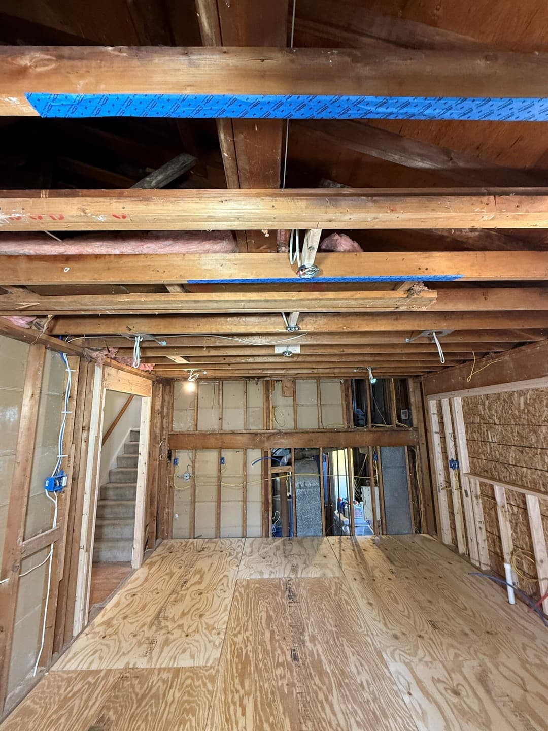 Exposed wooden beams and plywood flooring in a home renovation project interior.
