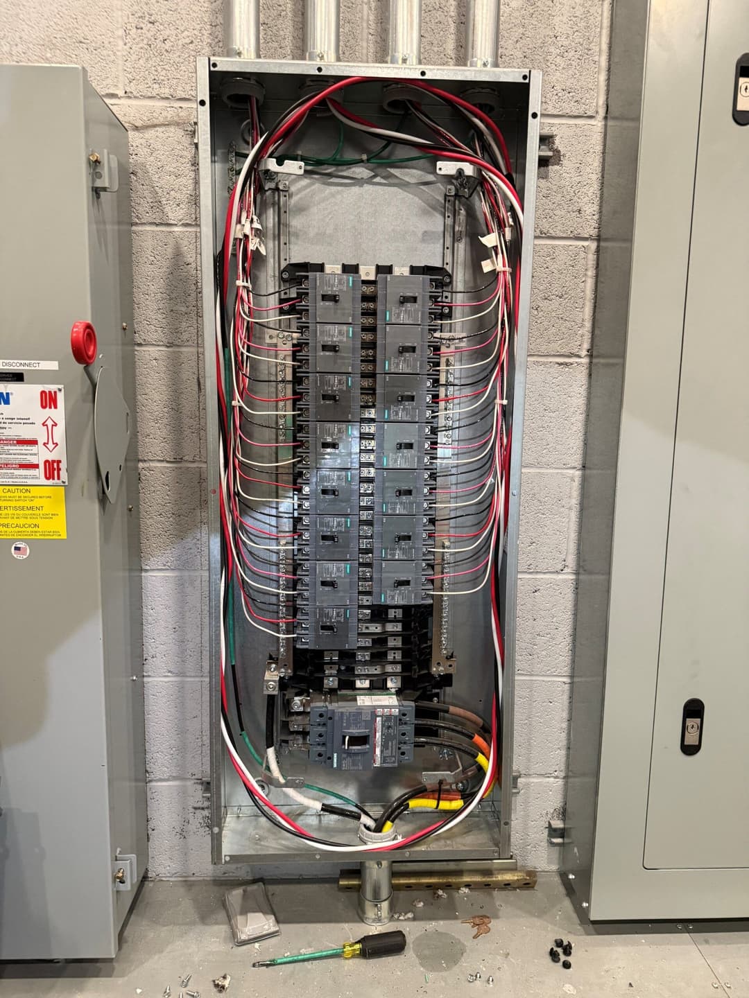 Electrical panel with circuit breakers and wiring in a gray utility room.