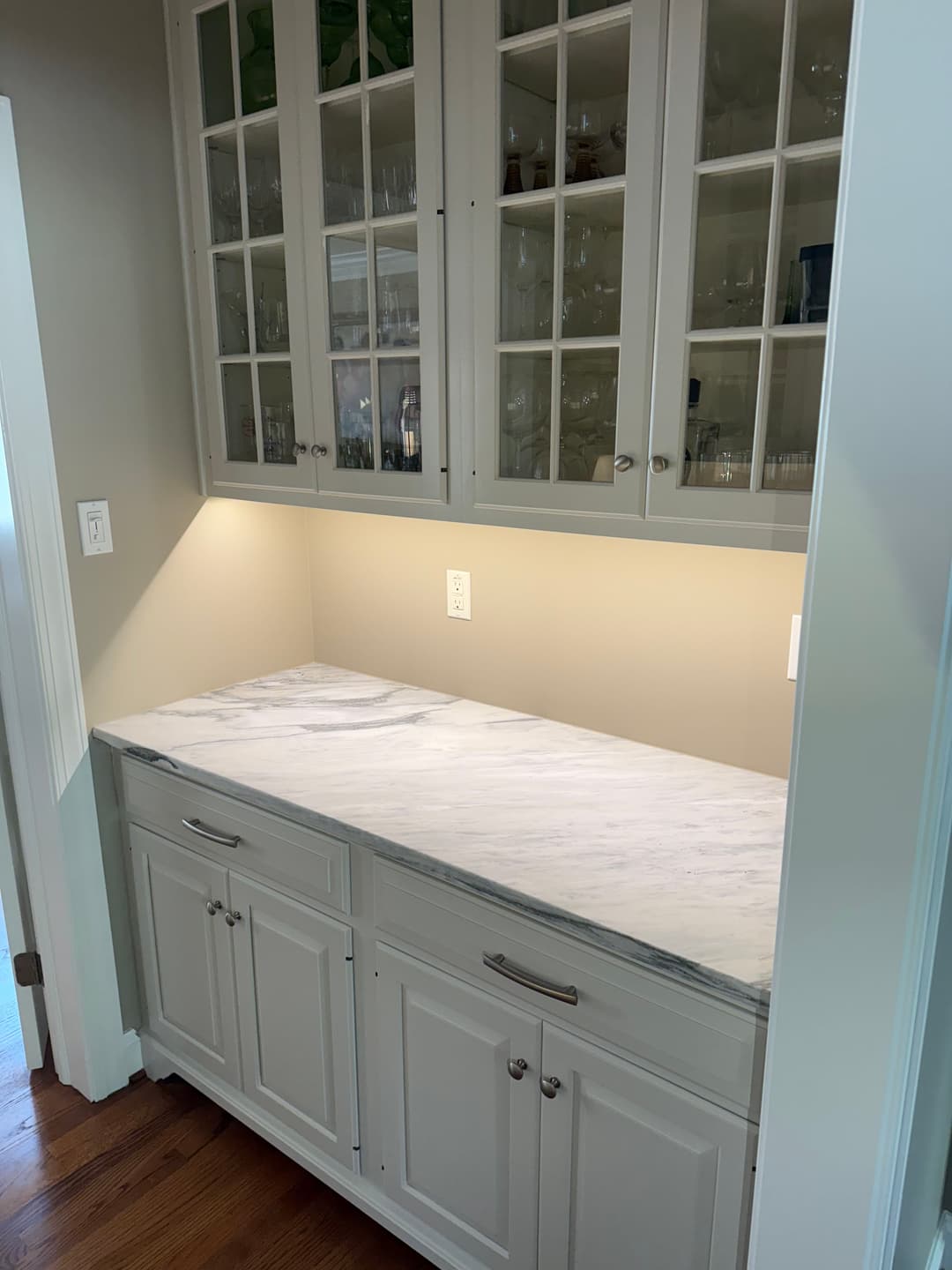 Modern kitchen countertop with marble surface and glass-front cabinetry, illuminated beneath.