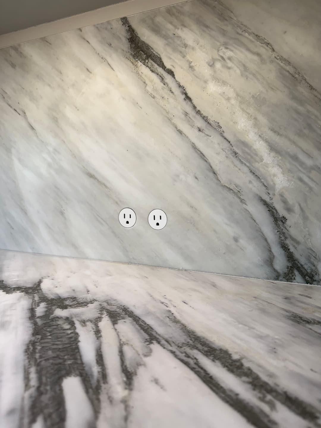 Marble wall with natural stone pattern and two electrical outlets.