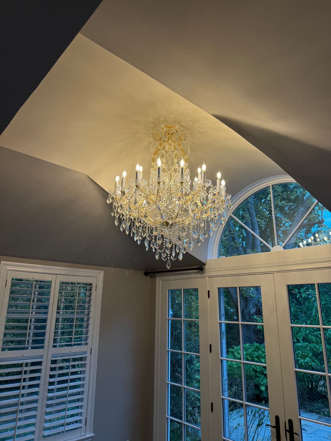 Elegant crystal chandelier hanging from a ceiling in a well-lit room with large windows.